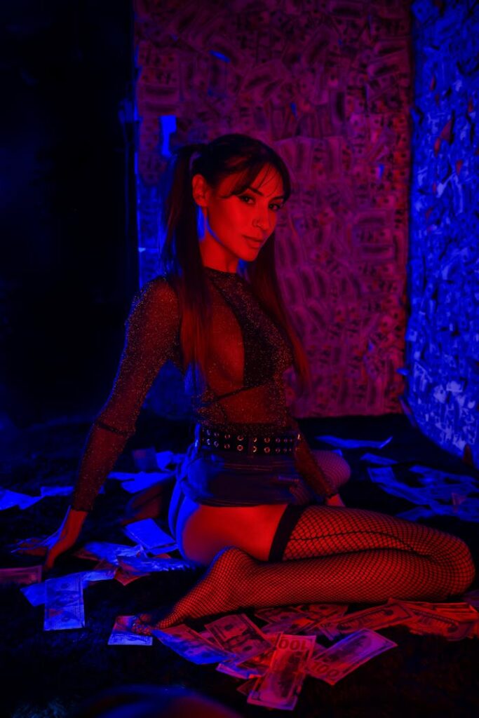 Woman posing in neon lighting surrounded by money and wearing fishnet stockings.