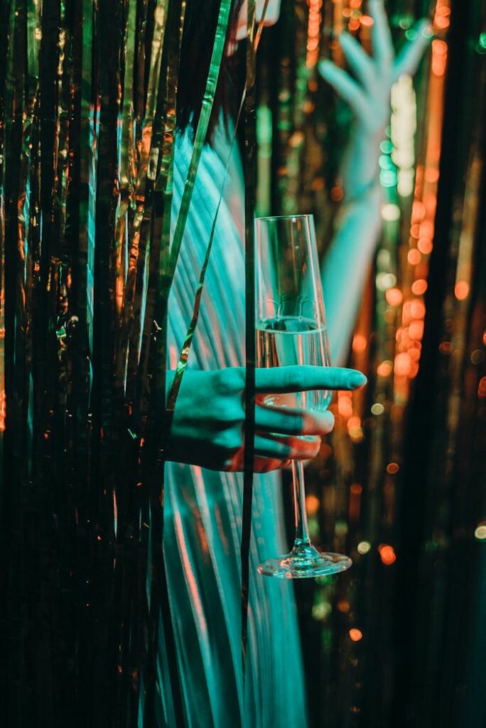 A stylish hand holds a champagne glass amidst a glittering party backdrop, exuding celebration vibes.